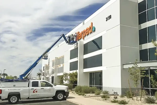 Painters using a lift from their truck to paint the logo on the side of a building, emphasizing meticulous workmanship and professional service.