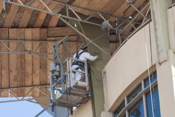 Painters using a lift to reach and paint the upper structure of a building, demonstrating precision and safety in their work.