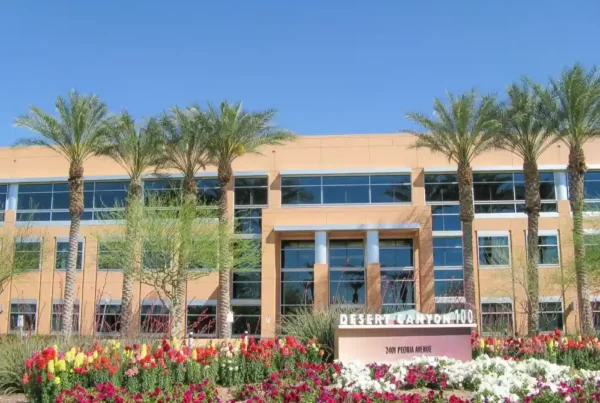 A commercial building surrounded by trees and flowers in the foreground, blending urban architecture with natural landscaping.