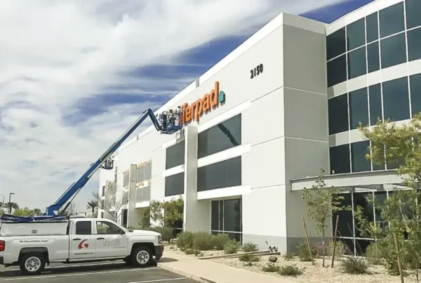 Painters using a lift from their truck to paint the logo on the side of a building, emphasizing meticulous workmanship and professional service.