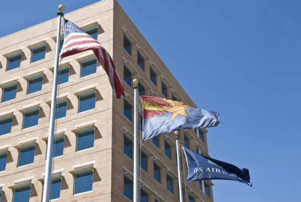 Three flags mounted on separate poles, waving in the breeze against a clear sky.