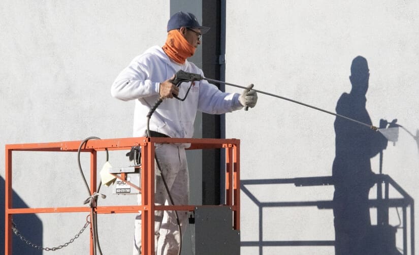 Guy is using a Commercial Paint Sprayer to paint the wall